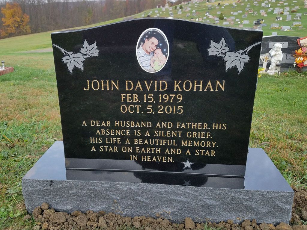 Black granite gravesite marker with white lettering and angel designs in a cemetery