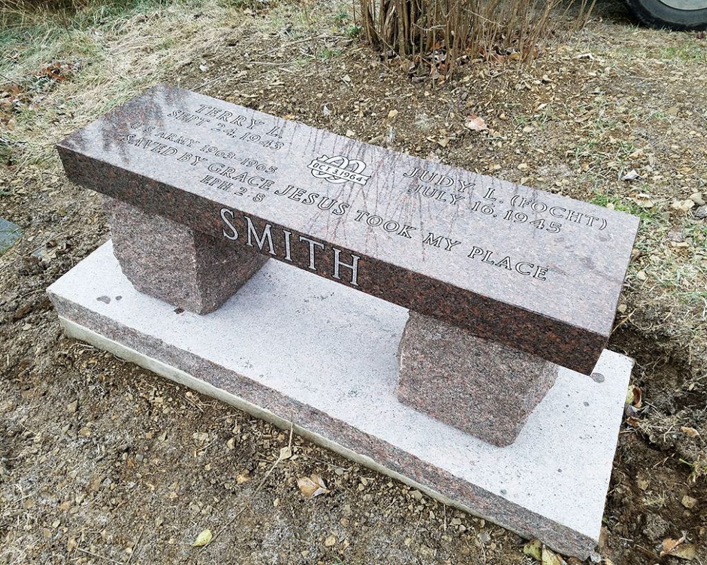 Stone bench with engraved text on a grassy outdoor ground, viewed at an angle