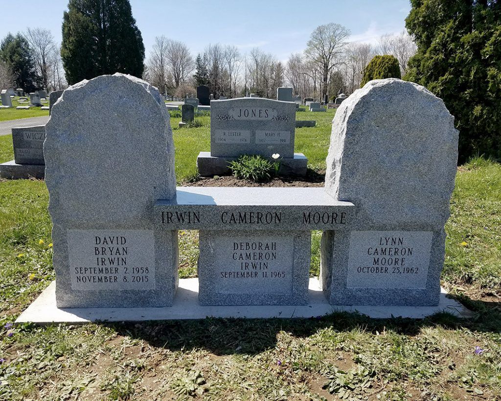 Three-part granite gravestone in a cemetery with engraved names and dates on a sunny day