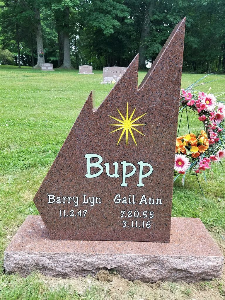Bupp memorial stone with yellow starburst and floral tribute in a grassy cemetery setting