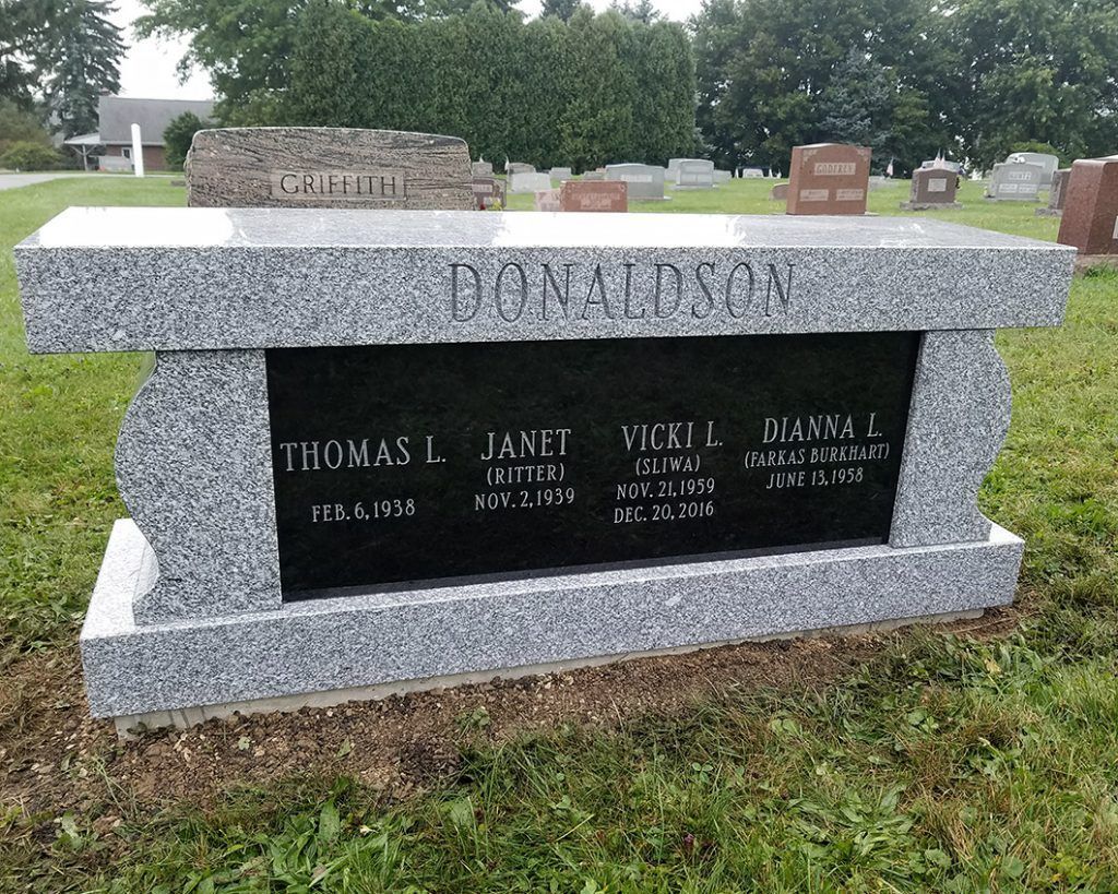 Gray granite family tombstone with engraved black center panel in a grassy cemetery.