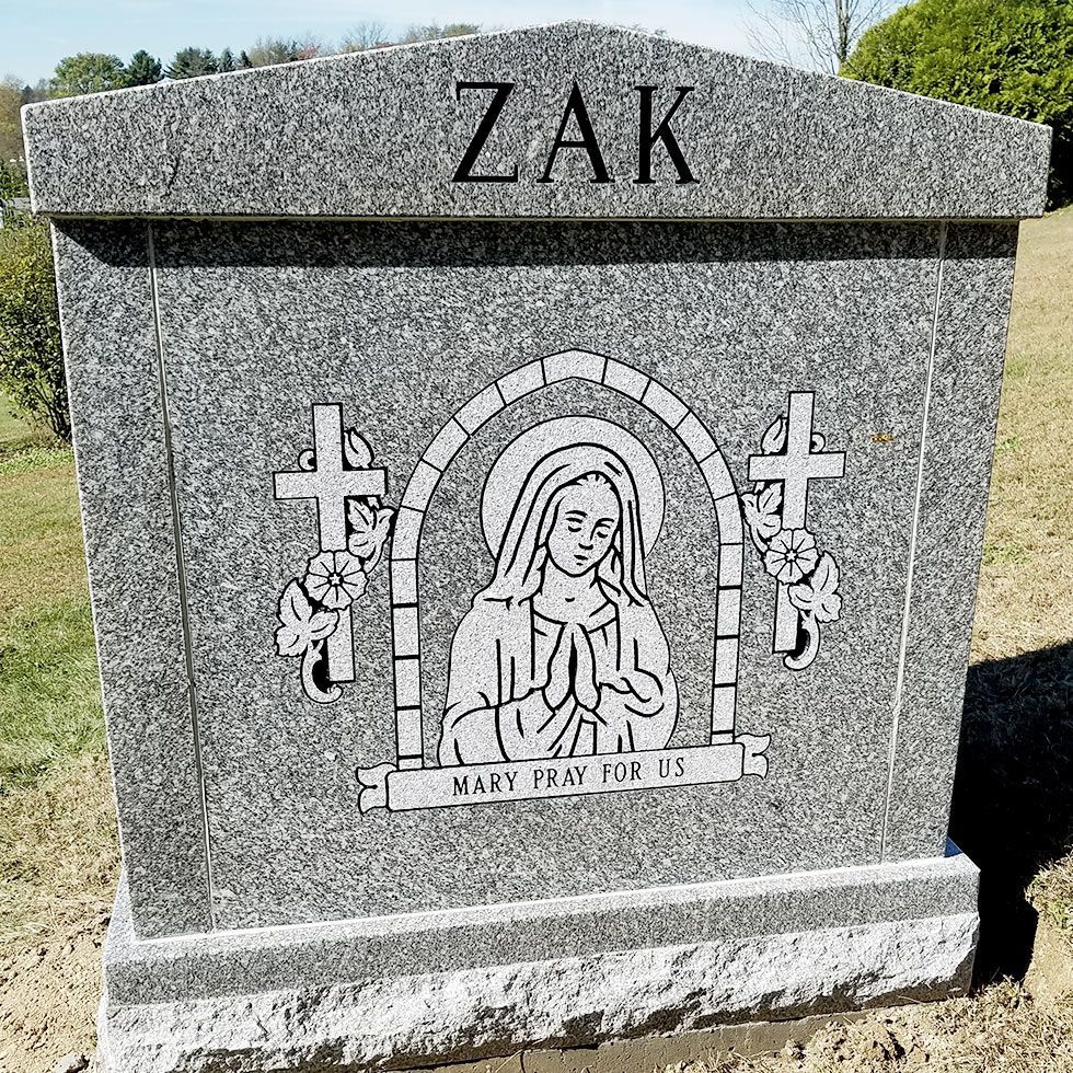 Gray granite gravestone engraved “ZAK” with a Mary statue and “Mary, pray for us” plaque
