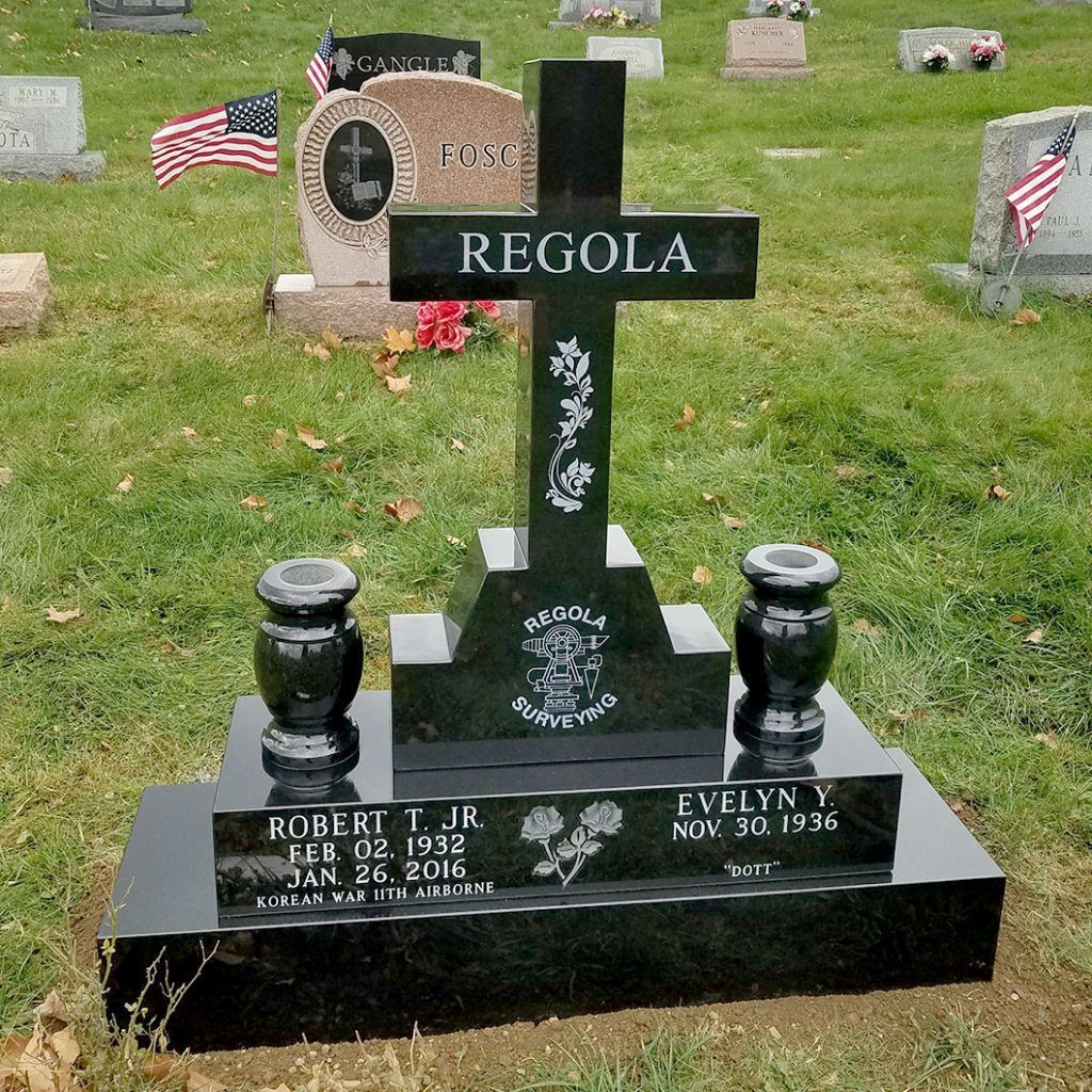 Black memorial gravestone with flowers in a cemetery, marked “REGOLA” with American flags nearby