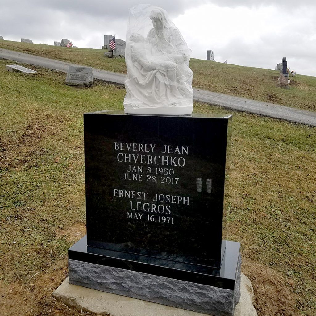 Black gravestone with white angel statue in a grassy cemetery hillside
