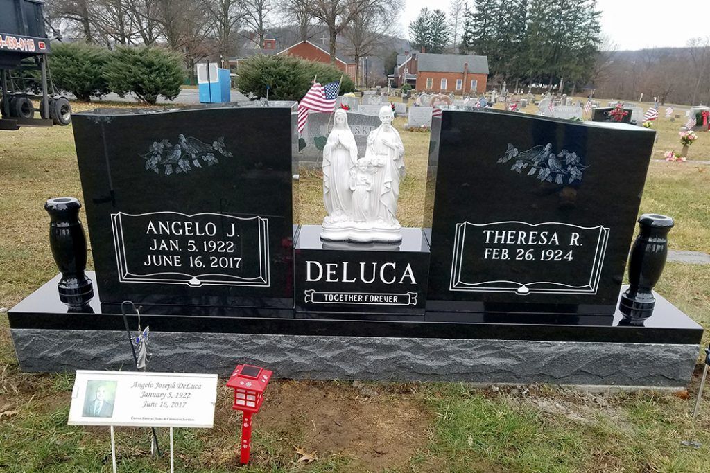 Black double gravestone with white angel statues and red flowers in a cemetery