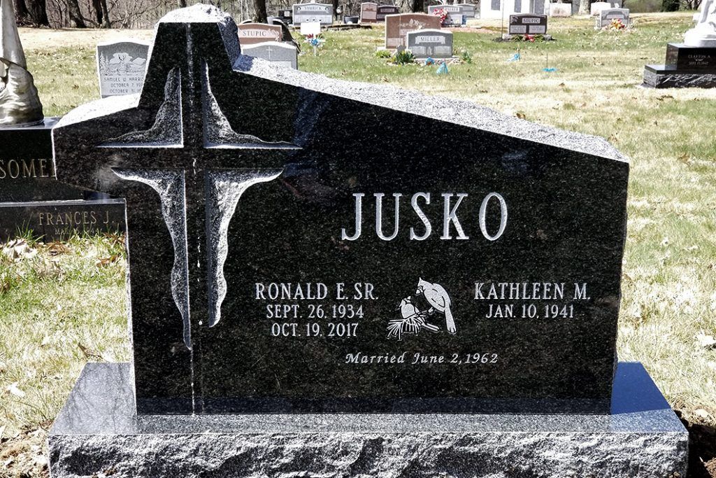Black granite gravestone with cross and the name JUSKO in a cemetery.