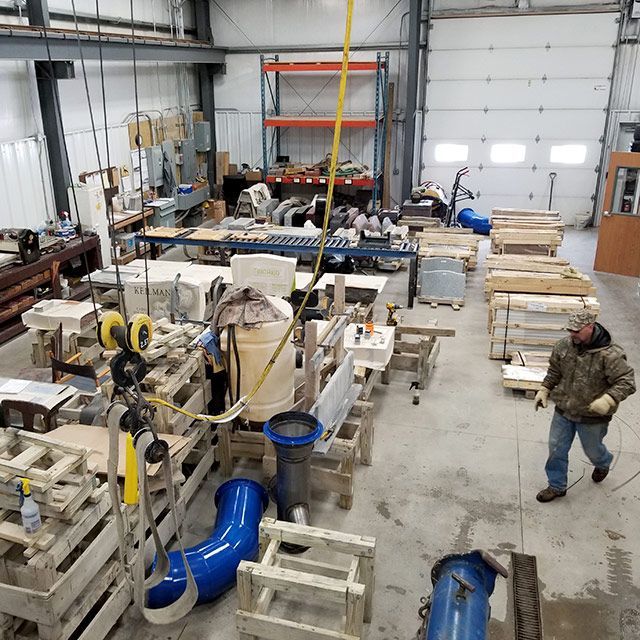 Industrial workshop with machinery, blue ventilation ducts, and a person walking near stacked materials