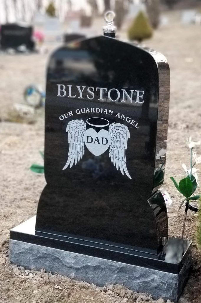 Black gravestone with “Blystone” and white angel wings at a cemetery.