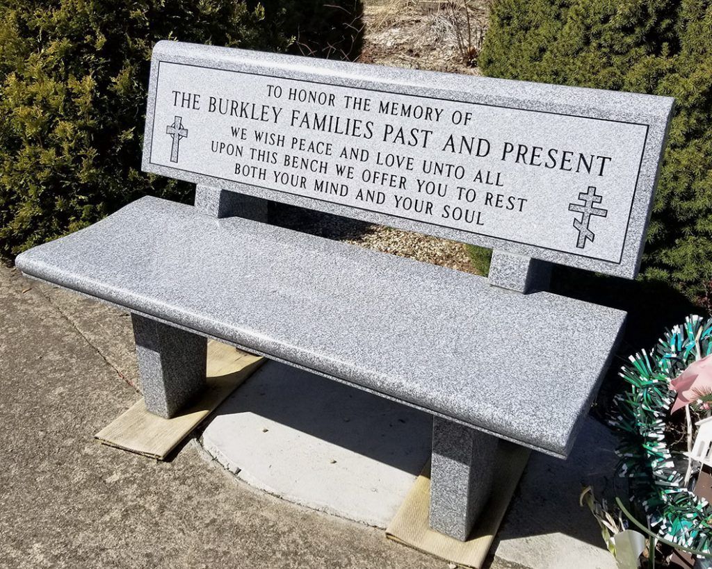 Gray memorial bench with engraved backrest in a cemetery or garden setting