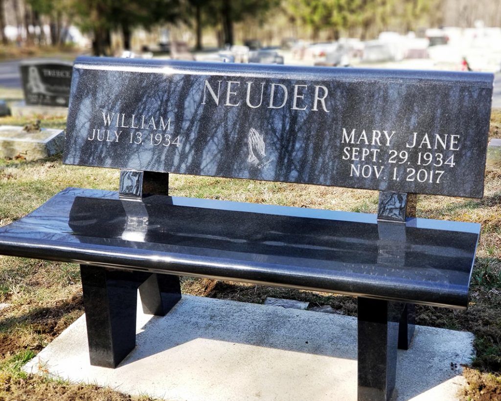 Black memorial bench grave marker engraved “NEUDER” and “MARY JANE,” in a cemetery.
