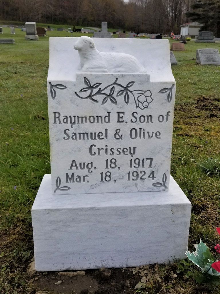 White gravestone with floral carving in a cemetery, engraved with “Raymond E. Son of Samuel & Olive,” dates 1917–1924.