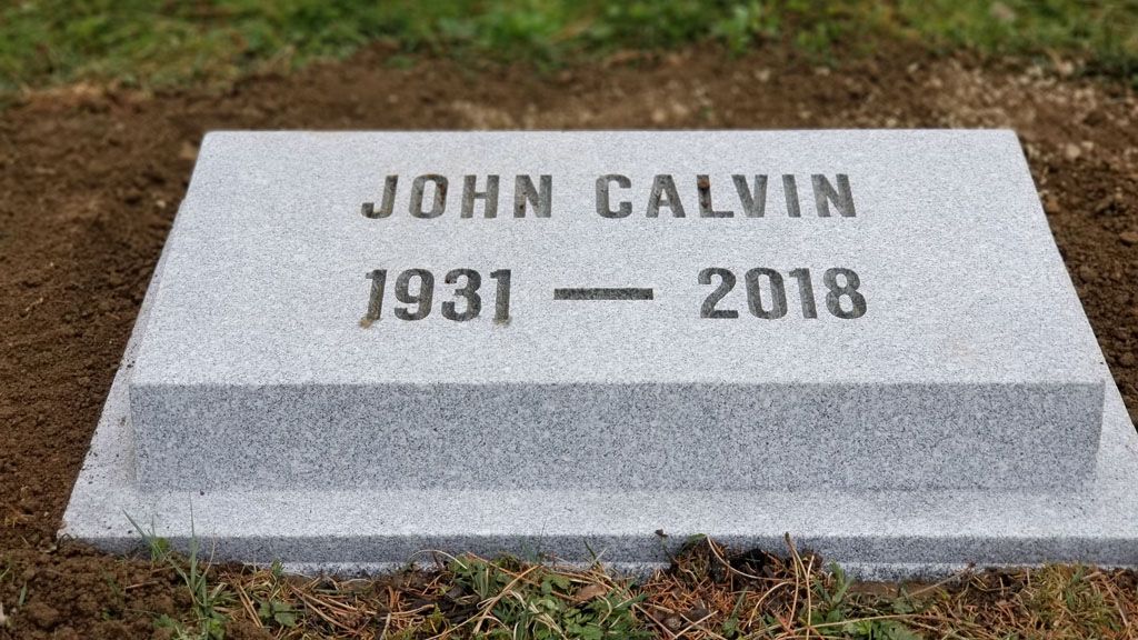 Gravestone reading “John Calvin, 1931–2018” on grass