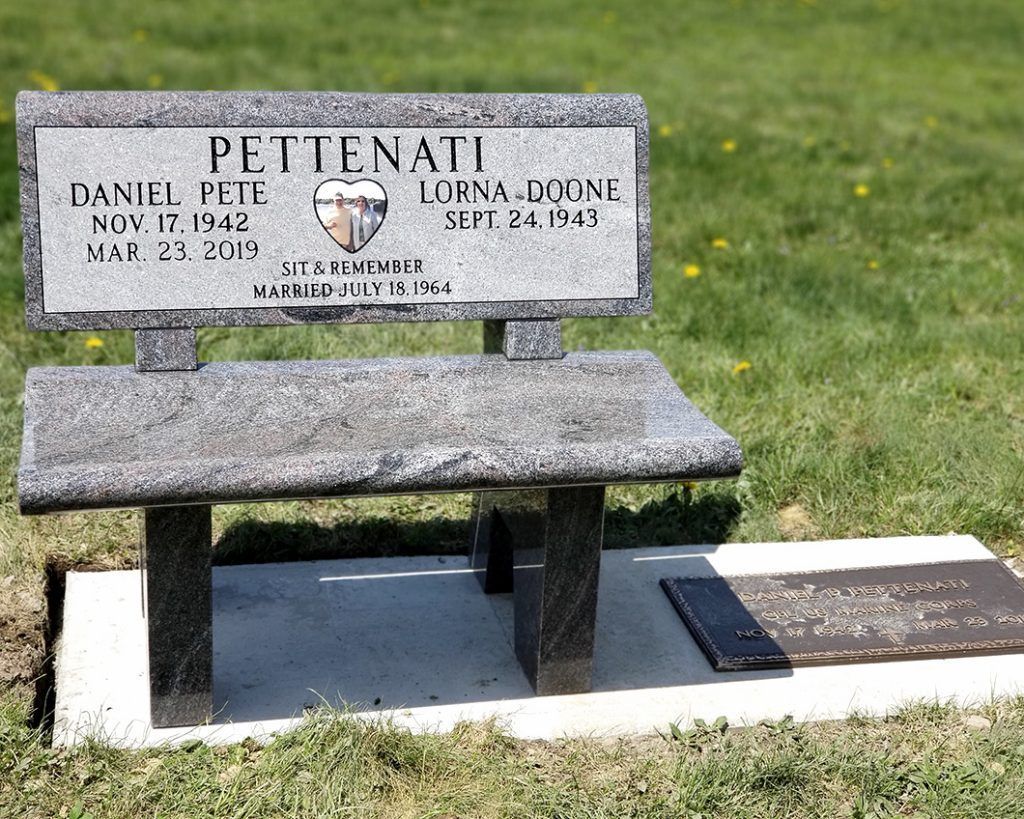 Memorial bench and gravestone for the Pettenati family on grass, with a bronze plaque nearby