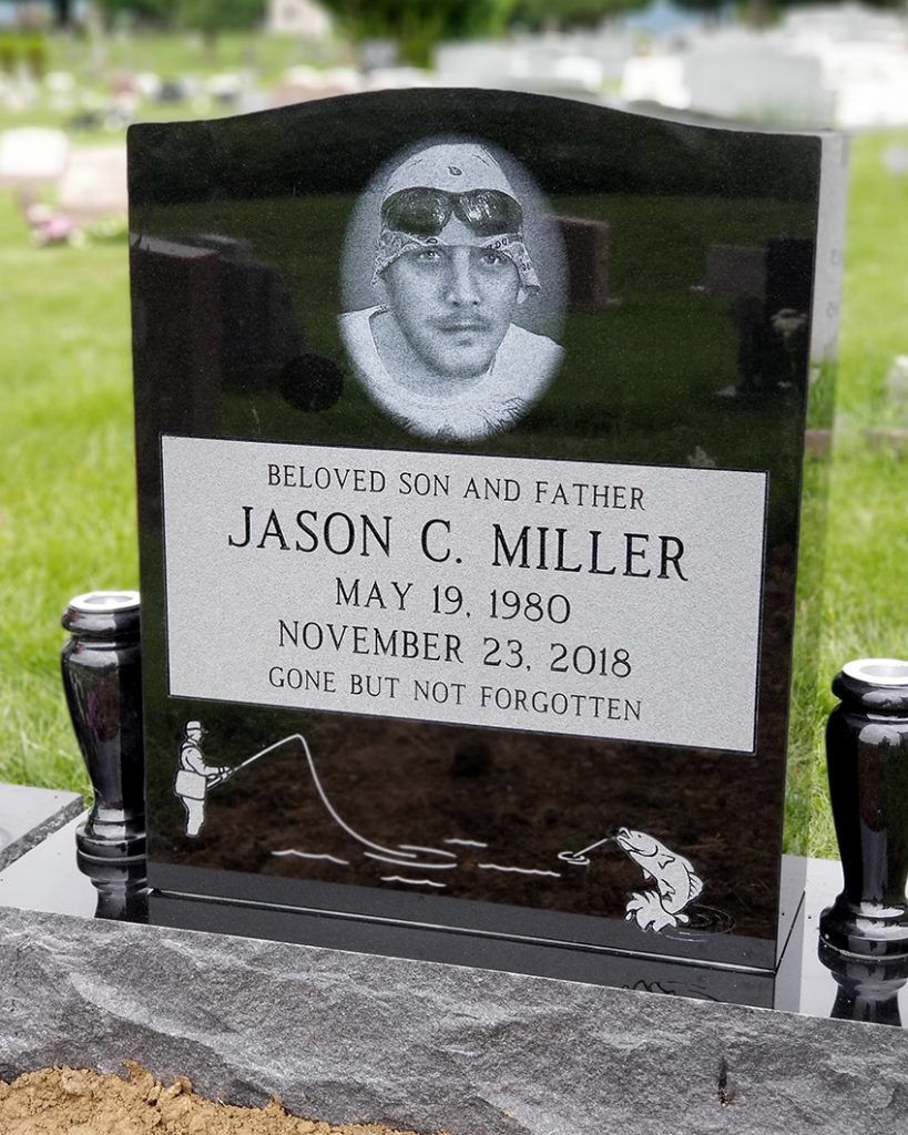 Glossy black gravestone with portrait etching and white plaque, set in a cemetery