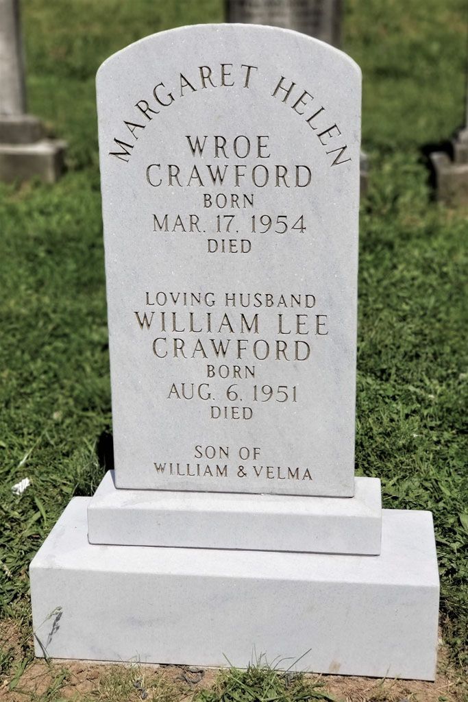 White gravestone in a cemetery with engraved memorial text and a stepped base.