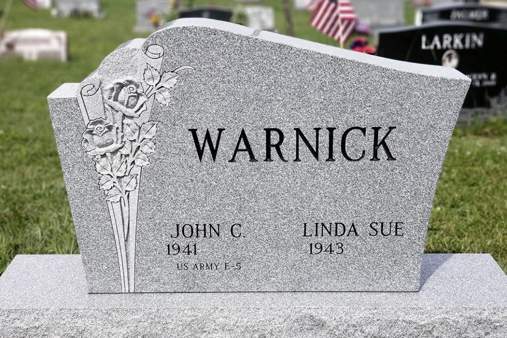 Gray granite gravestone engraved “WARNICK” in a cemetery, with floral carving and two smaller names below