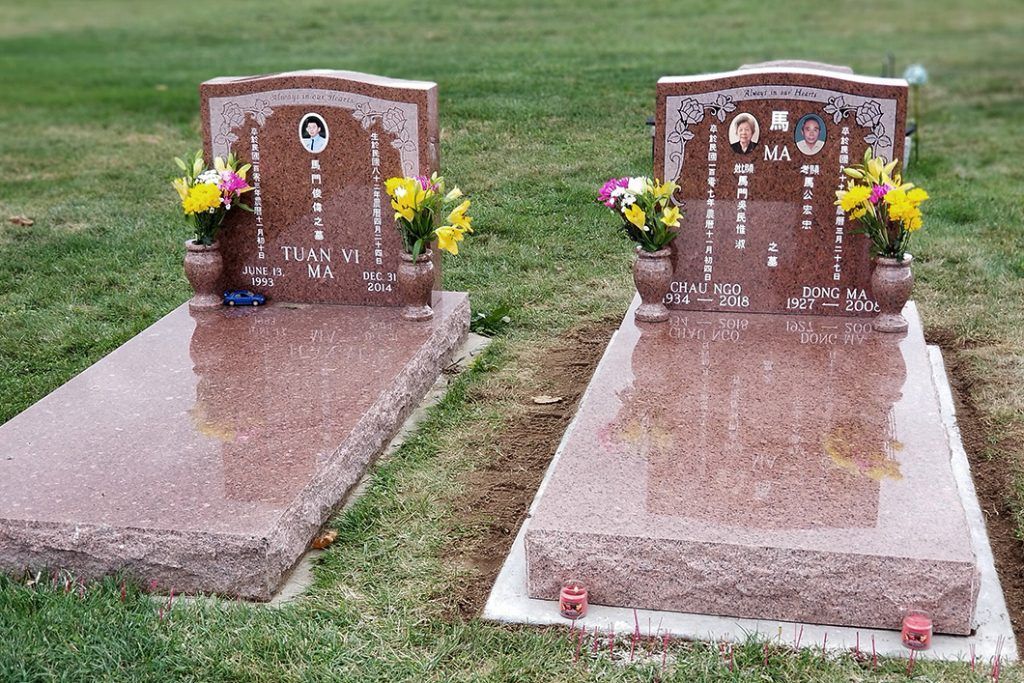 Two polished granite gravestones with flower vases in a grassy cemetery.