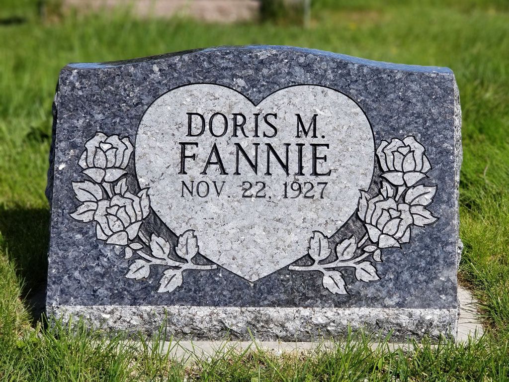 Gray granite gravestone with heart and floral carvings reading “Doris M. Fannie, Nov 22 1927.”