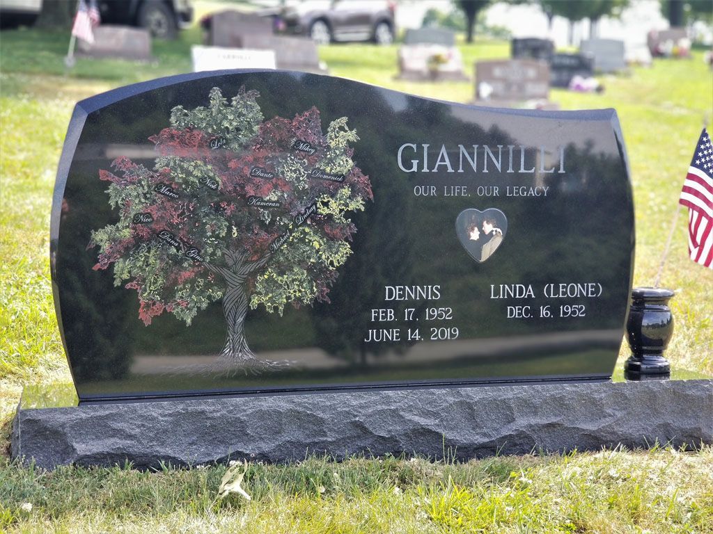 Black granite gravestone with tree engraving and U.S. flag in a cemetery