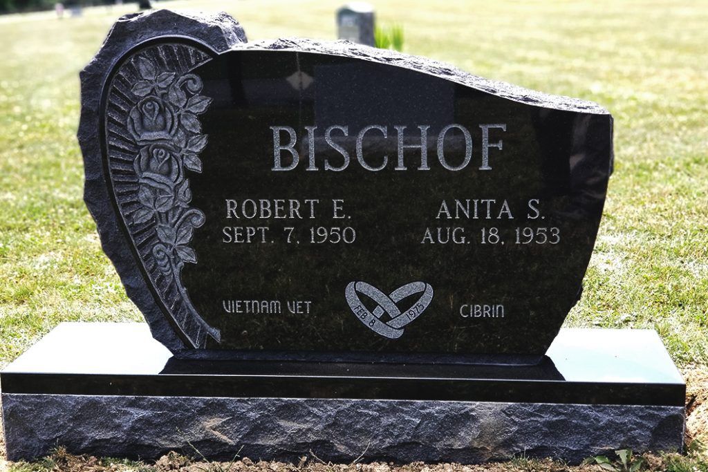 Black gravestone with floral carving and the name Bischof in a sunny cemetery