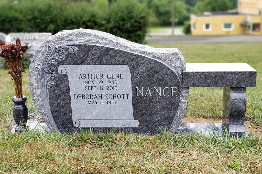 Granite memorial bench with vase of flowers in a grassy cemetery yard