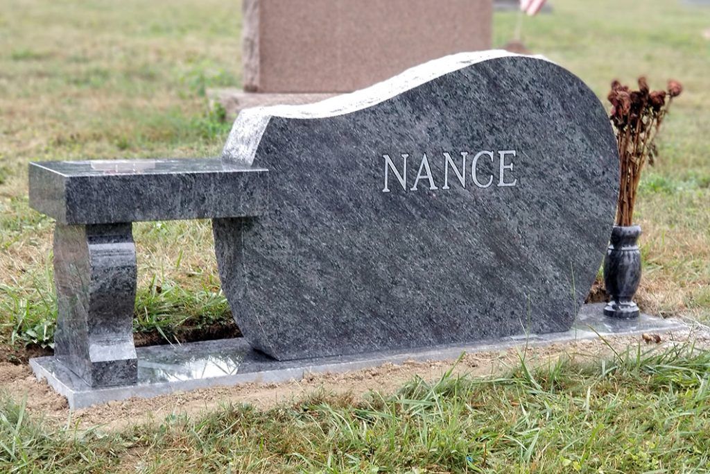 Gray granite gravestone shaped like a bench with the name “NANCE” engraved on it.
