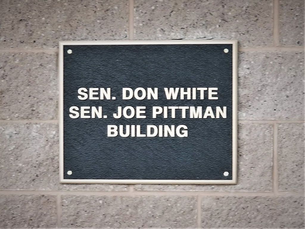 Plaque on brick wall reading “Sen. Don White Sen. Joe Pittman Building”