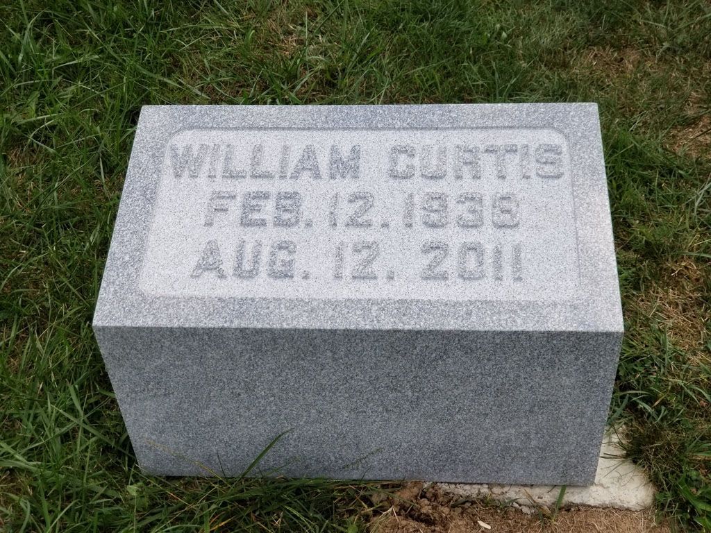 Gray granite gravestone on grass with engraved name and dates