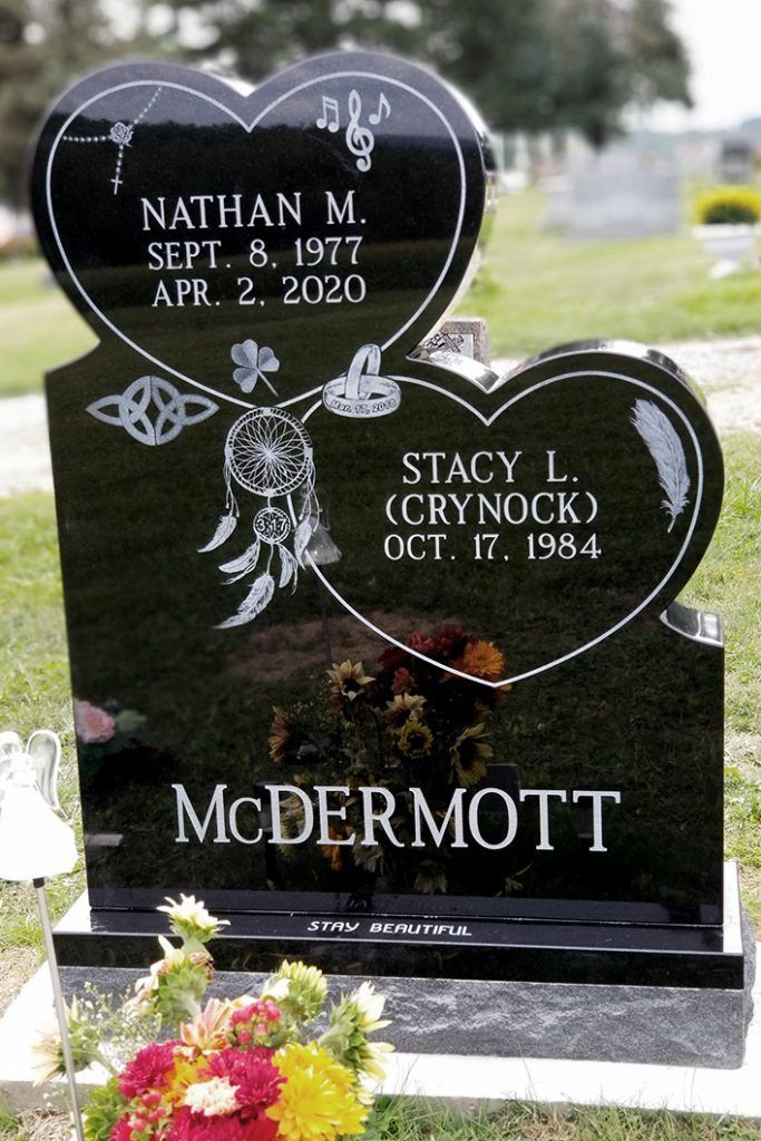 Black heart-shaped double gravestone with flowers at its base in a cemetery, engraved McDermott and names/dates