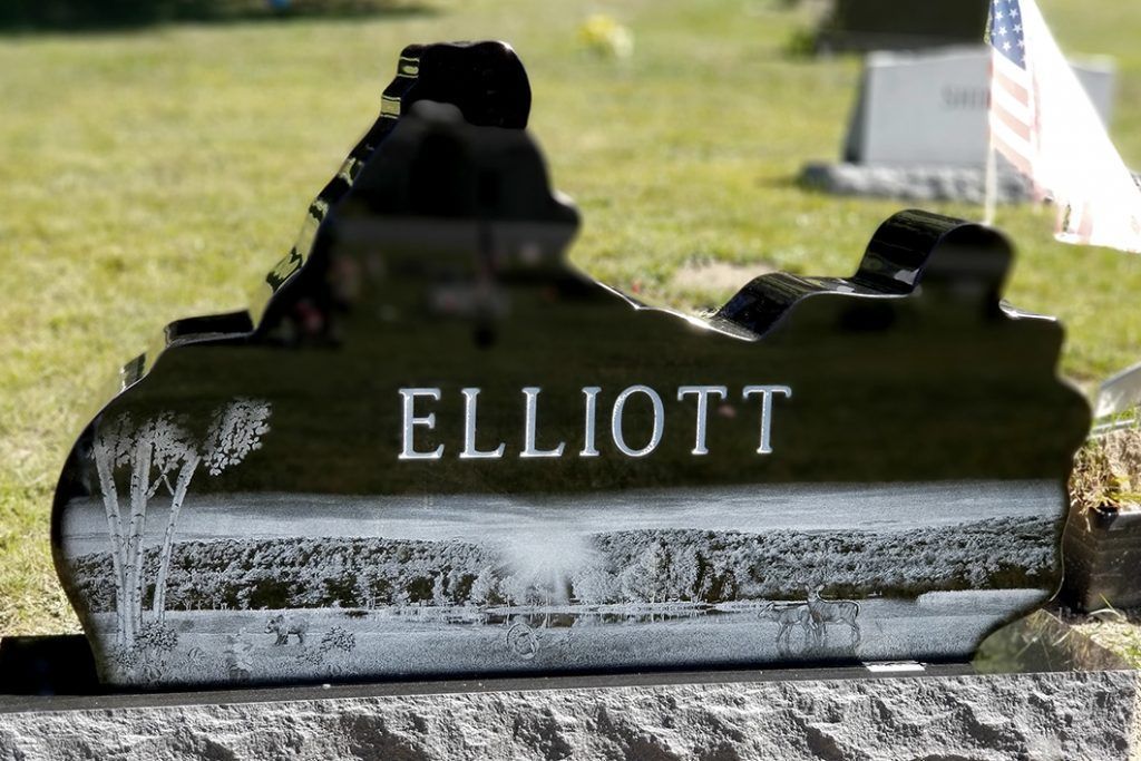 Elliott engraved on a weathered black gravestone in a grassy cemetery