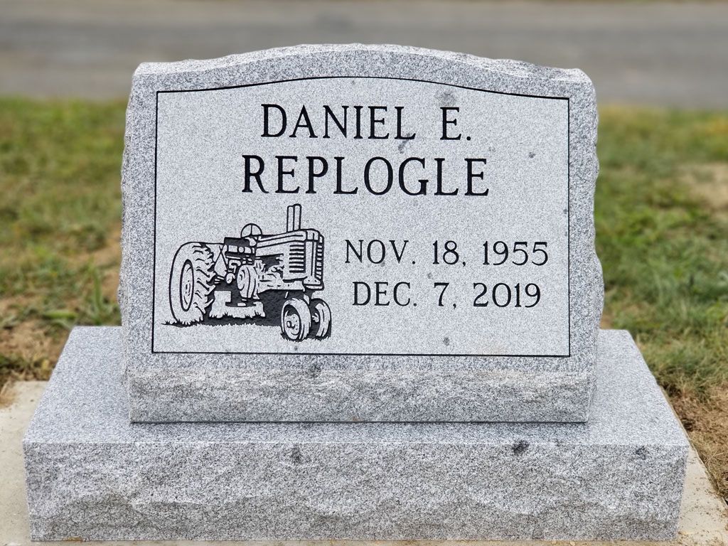 Gray granite gravestone for Daniel E. Replogle with a tractor engraving and dates Nov. 18, 1952–Dec. 7, 2019