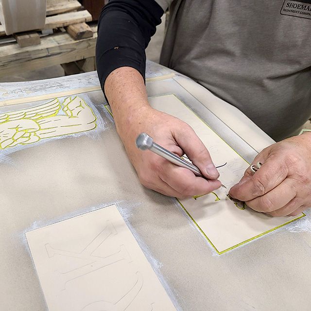 Hands tracing a yellow pattern onto white fabric on a worktable