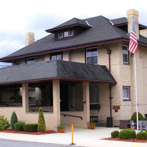 Two-story beige house with a dark roof, front porch, and an American flag by the entrance