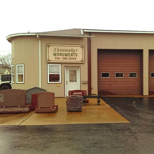 Schoenmaker Monuments storefront with tan exterior, garage bays, and stone memorial displays outside