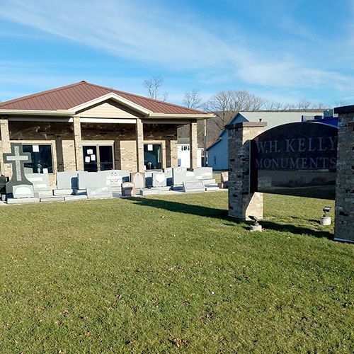 Stone monument shop with gravestones displayed outside a brick building on a sunny day