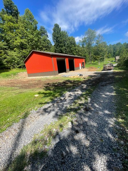 Red barn with open doors and gravel driveway on a sunny day.