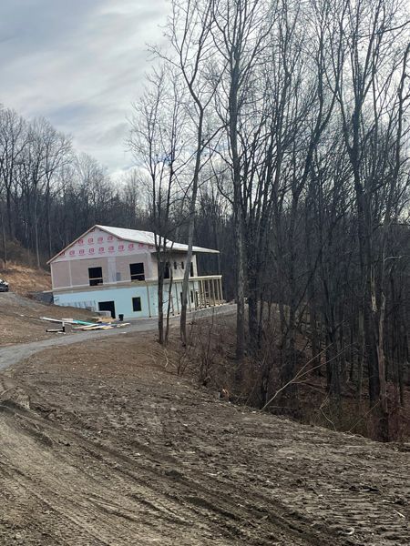 Building under construction in a wooded area, with dirt road leading to the site.