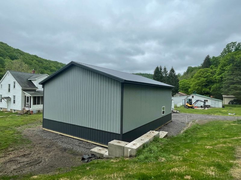 A new gray and black metal barn in a rural setting with a cloudy sky.