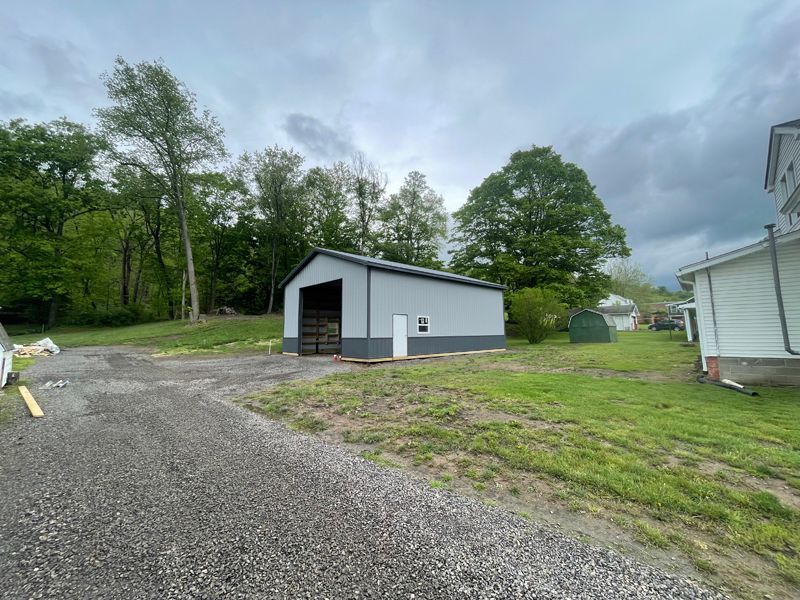 Gray metal storage building with black roof and white door, on a grassy lot.