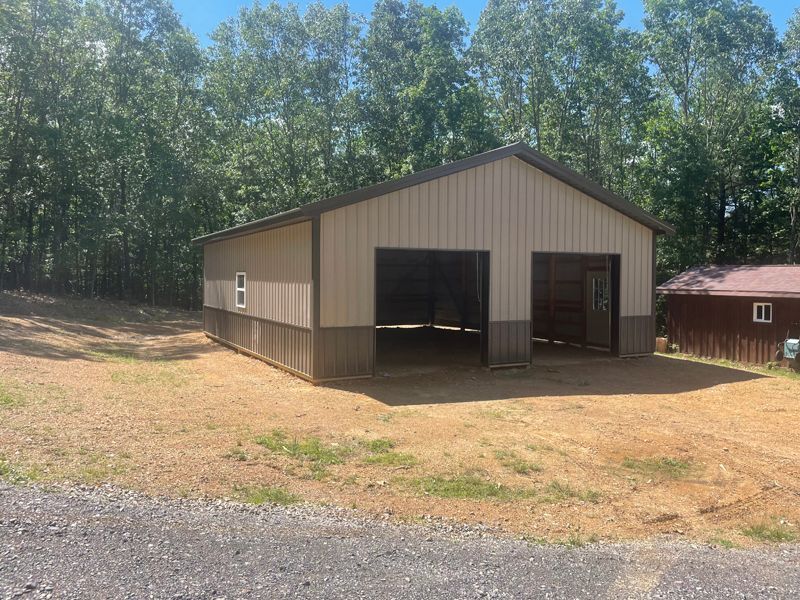 Tan and brown metal garage with two bays, set on a gravel area, surrounded by trees.