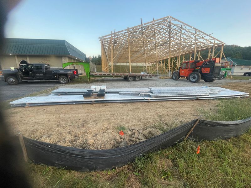 Construction site with a partially built wooden structure, truck, trailer, and panels on the ground.