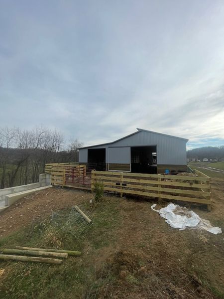 Barn with metal roof, wood fence, and cloudy sky.