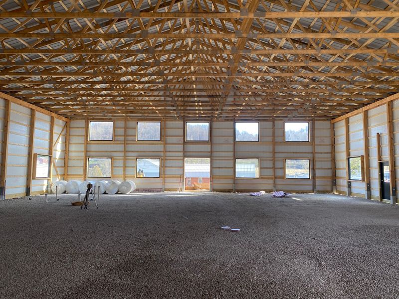Interior view of a large, unfinished barn with wooden beams and windows, filled with gravel flooring.