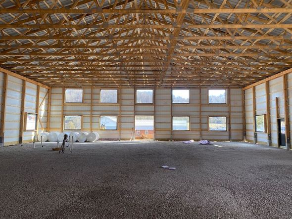 Interior view of a large, unfinished barn with wooden beams and windows, filled with gravel flooring.