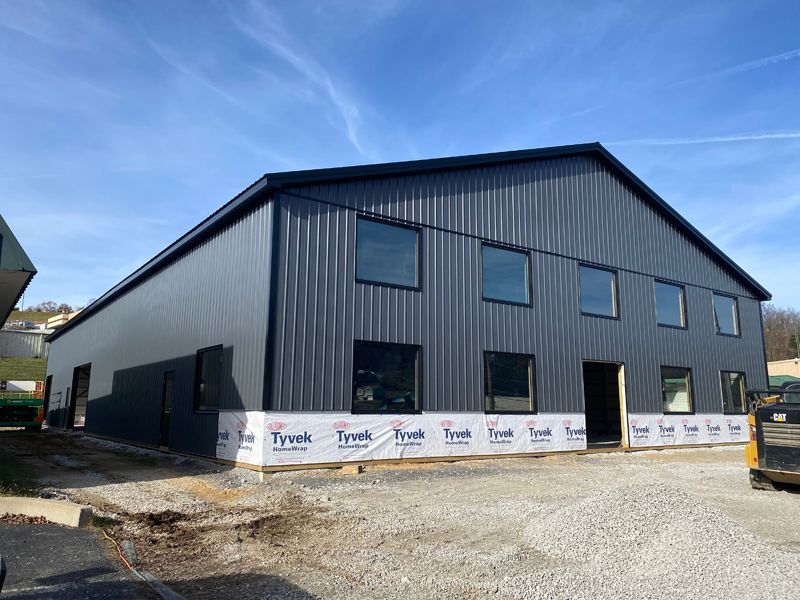 Dark gray metal building under construction, with windows and Tyvek wrap. Blue sky above.