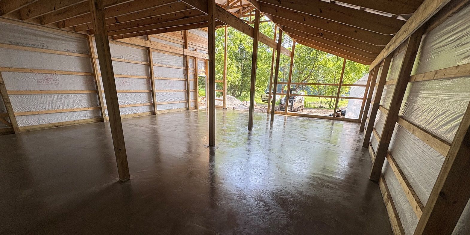 Inside of a partially constructed wooden building with a wet concrete floor, view towards the open side.