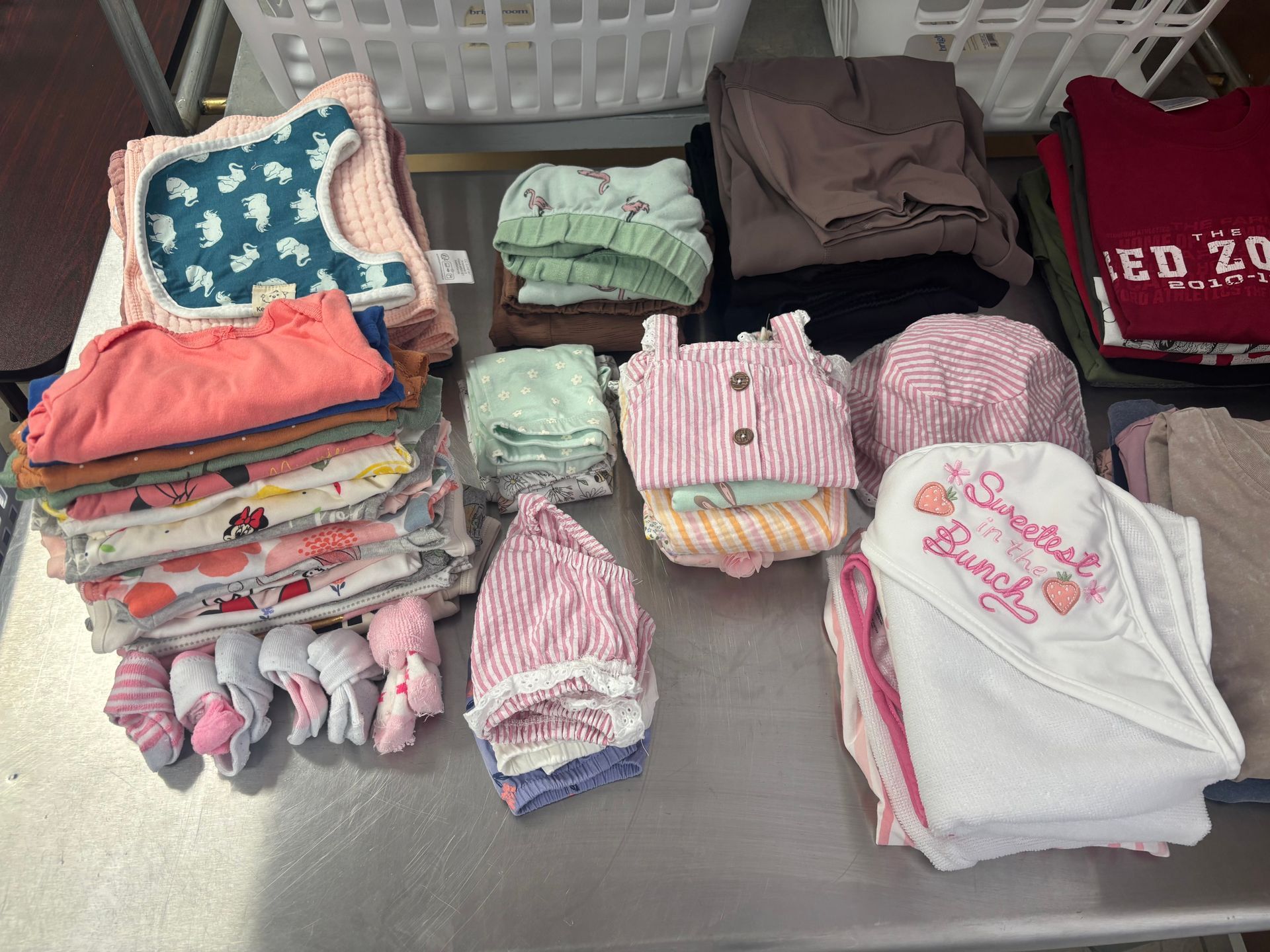 Stacks of baby clothes in various colors, including pink, blue, and green, on a metal surface.