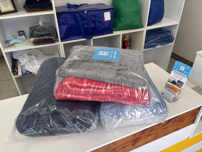 Wrapped blankets on a table, shelves with storage bags in background.