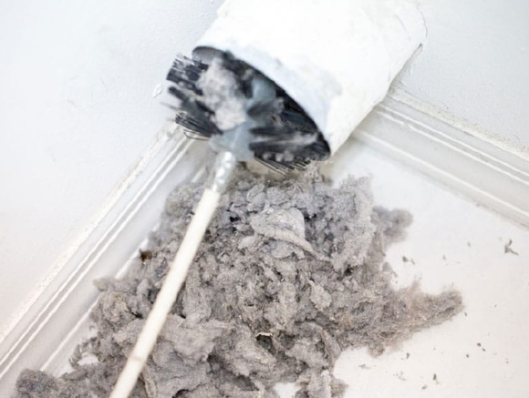 Broken white vacuum cleaner with gray lint spilled on a white floor.