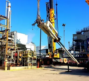 A large yellow crane is lifting a large pipe